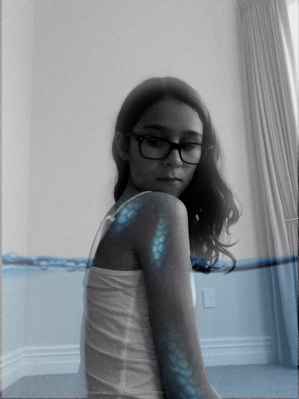 poorly edited black and white photo of me looking dramatically down with edited blue scales on my shoulders and blue surface of water behind me