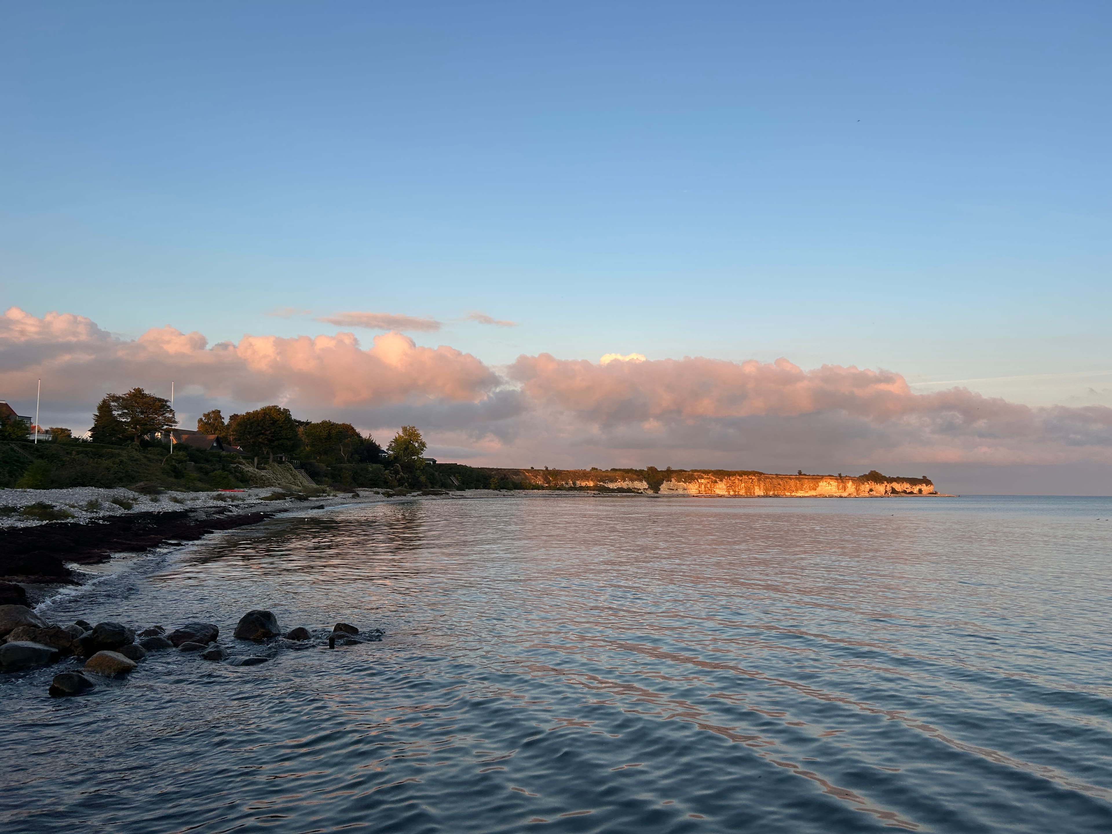rocky ocean shore and orange sunlight illuminating distant cliffs in rodvig, denmark