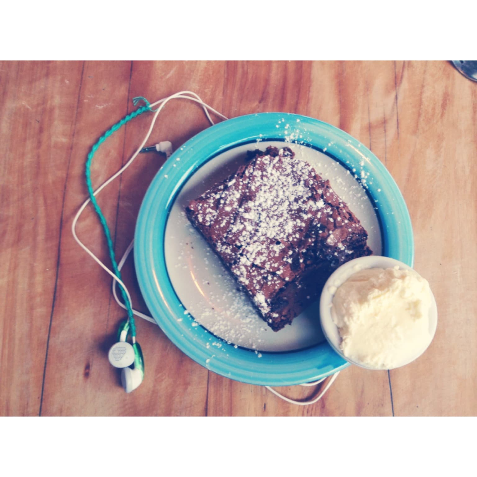aesthetically pleasing picture of sugar-dusted brownie on a plate with headphones wrapped under plate with white border and a hazy filter