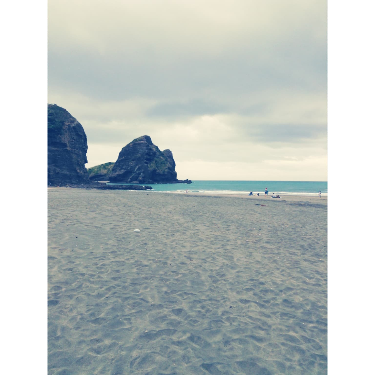 photo of black sand beach in new zealand with a white border and a hazy filter